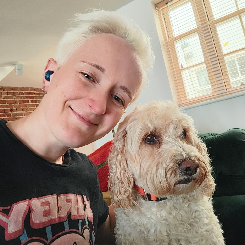 A person smiling for a selfie with a dog, both appearing relaxed at home.